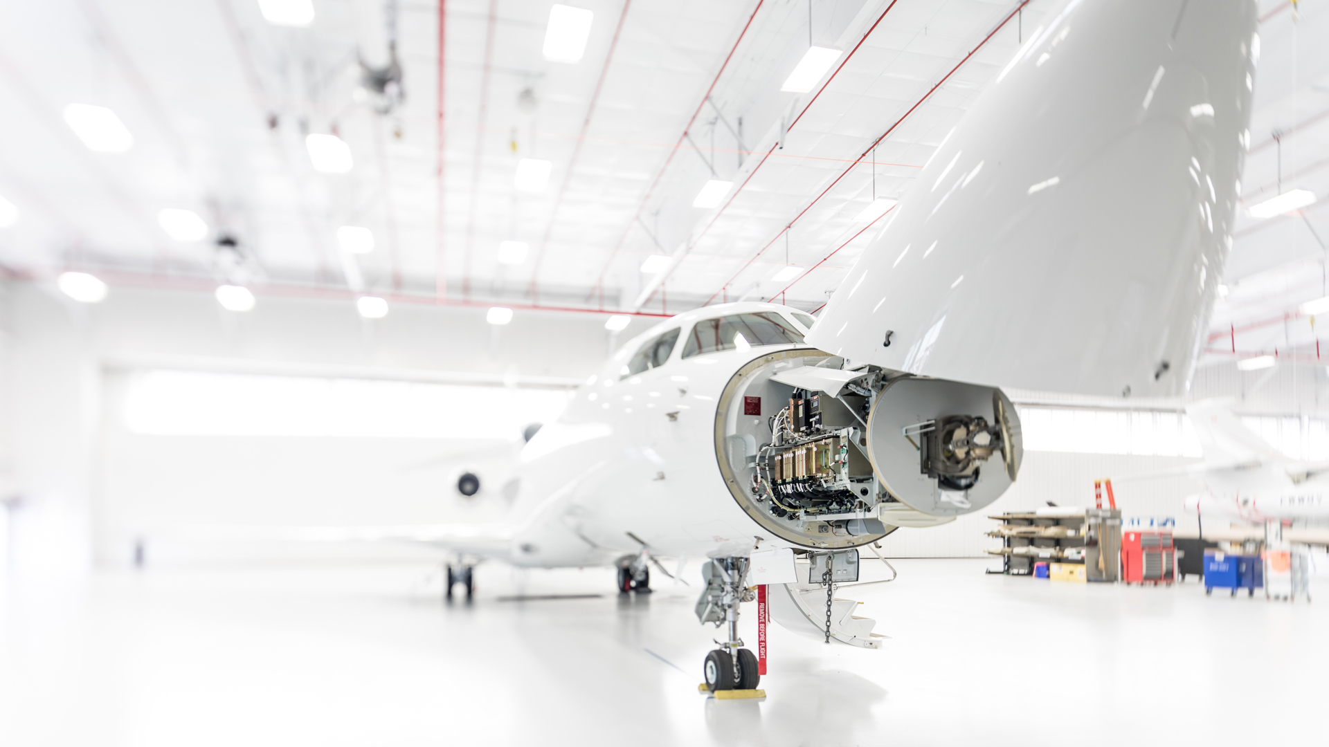 Luxury business jet in a bright white hangar with its nose cone open.