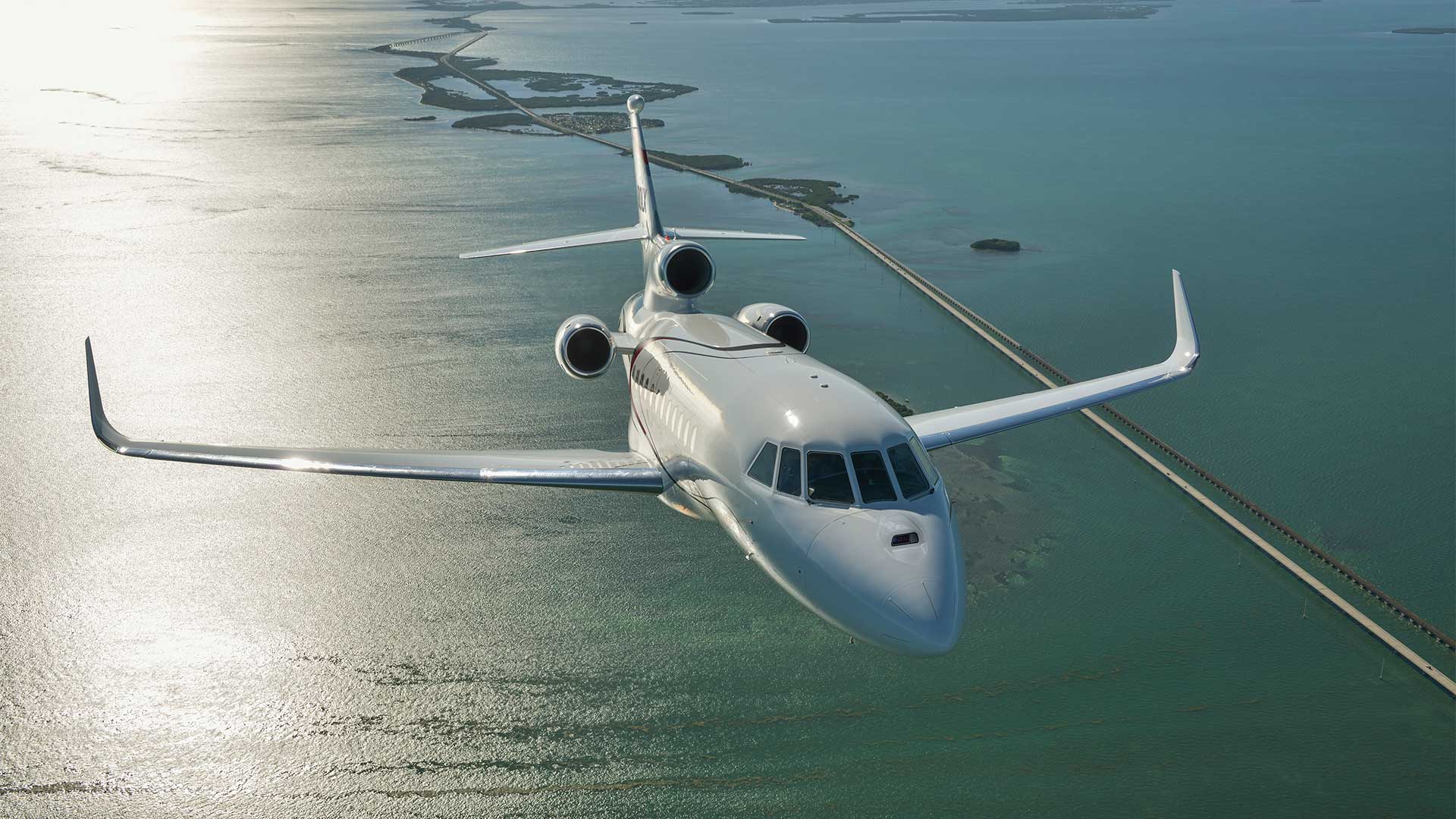 A Falcon 900LX flies over tropical water and islands.